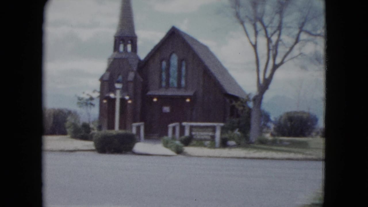1959 Nevada church exterior seen from across the street, with a dark wooden facade, steeple, bare trees, and low landscaping.