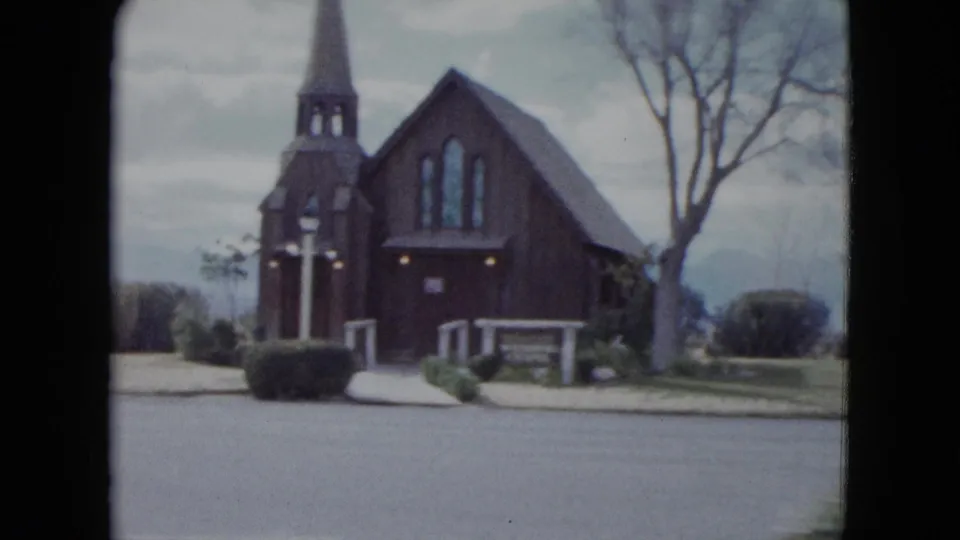 1959 Nevada church exterior seen from across the street, with a dark wooden facade, steeple, bare trees, and low landscaping.