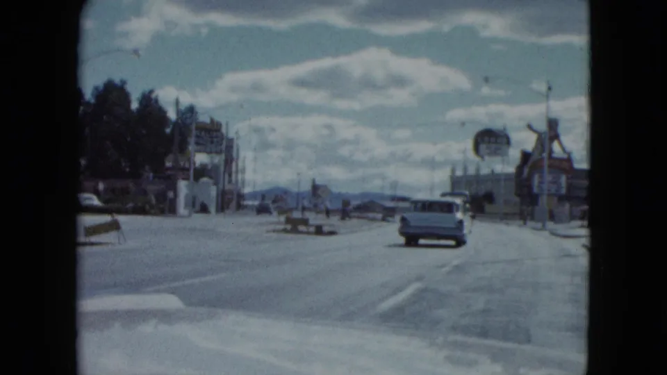 1959 Nevada home-movie view down a wide street with classic cars, commercial signs, utility poles, and mountains in the distance.