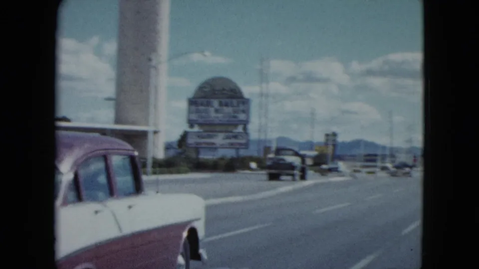 1959 Nevada street scene with a two-tone classic car, wide lanes, distant hills, and a large Flamingo roadside sign.