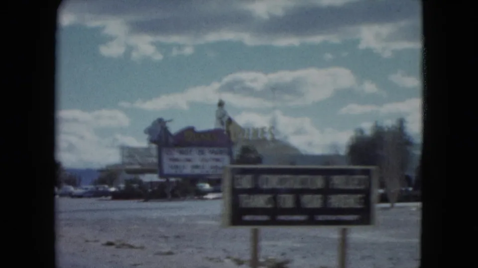 1959 Nevada home-movie view of a Dunes Hotel roadside sign advertising Nuit de Paris, with parked cars and low buildings nearby.
