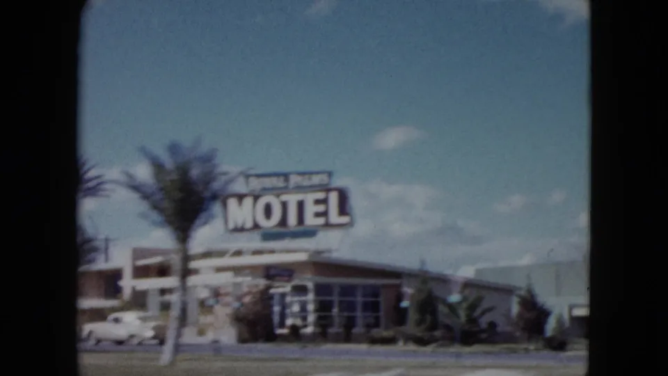 1959 Nevada roadside motel view with a large motel sign, palm tree, low building, parked cars, and bright sky.
