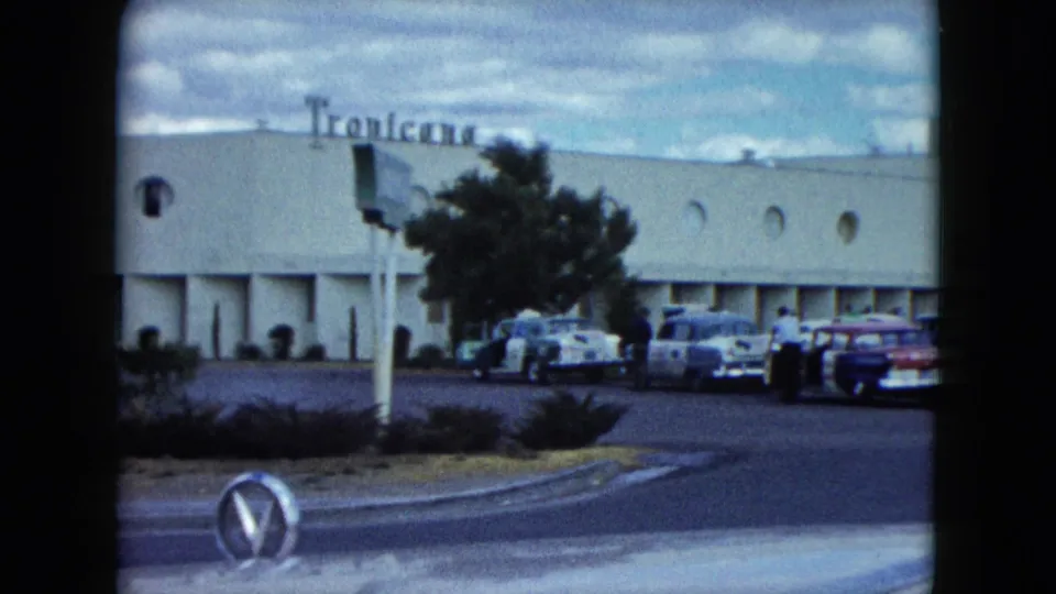 1959 Nevada home-movie frame showing a Tropicana exterior, parked late-1950s cars, rounded frame edges, and a roadside foreground.