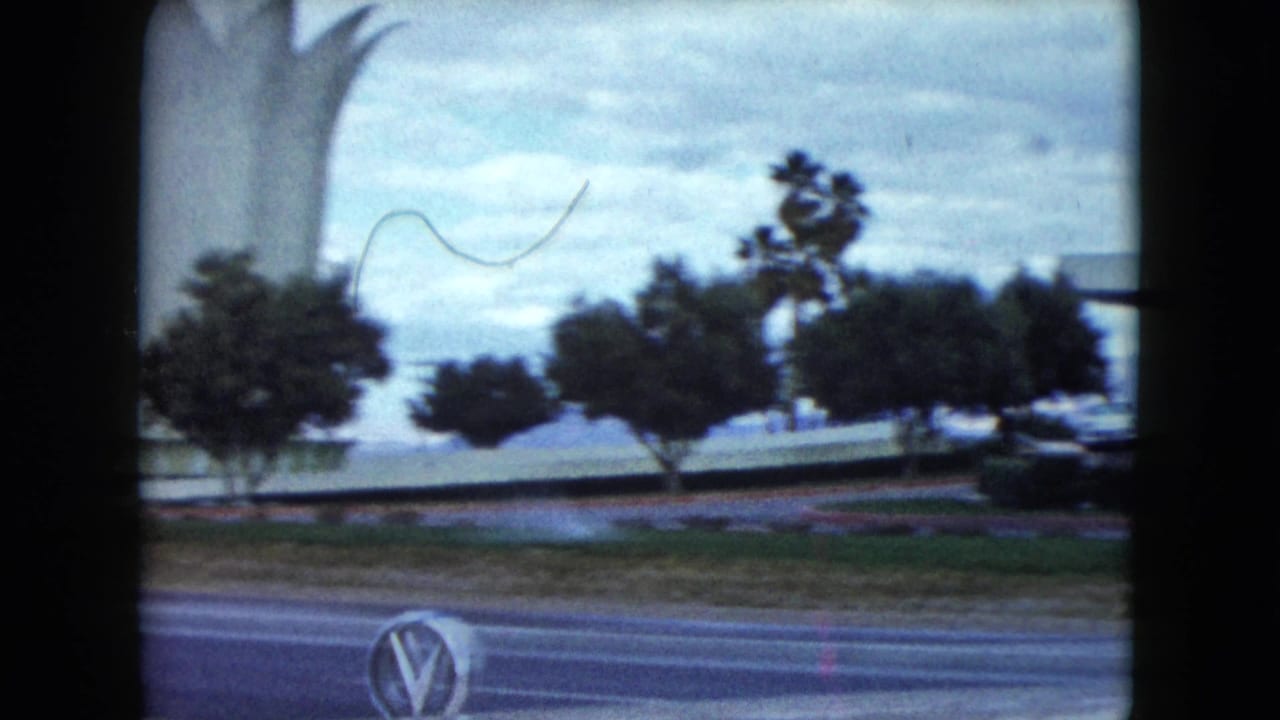 White sculptural monument beside a road, with trees and a car nearby.