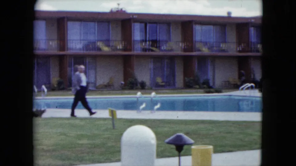 A man in a light shirt and dark pants walks along a Nevada poolside walkway in front of a two-story motel or apartment building.