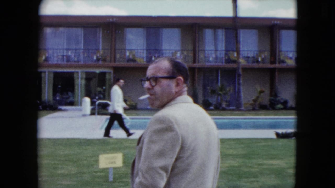 A 1959 Nevada motel pool scene shows a smoking man close to camera, with balcony rooms and a guest walking along the poolside path.