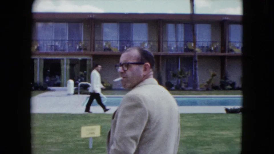 A 1959 Nevada motel pool scene shows a smoking man close to camera, with balcony rooms and a guest walking along the poolside path.