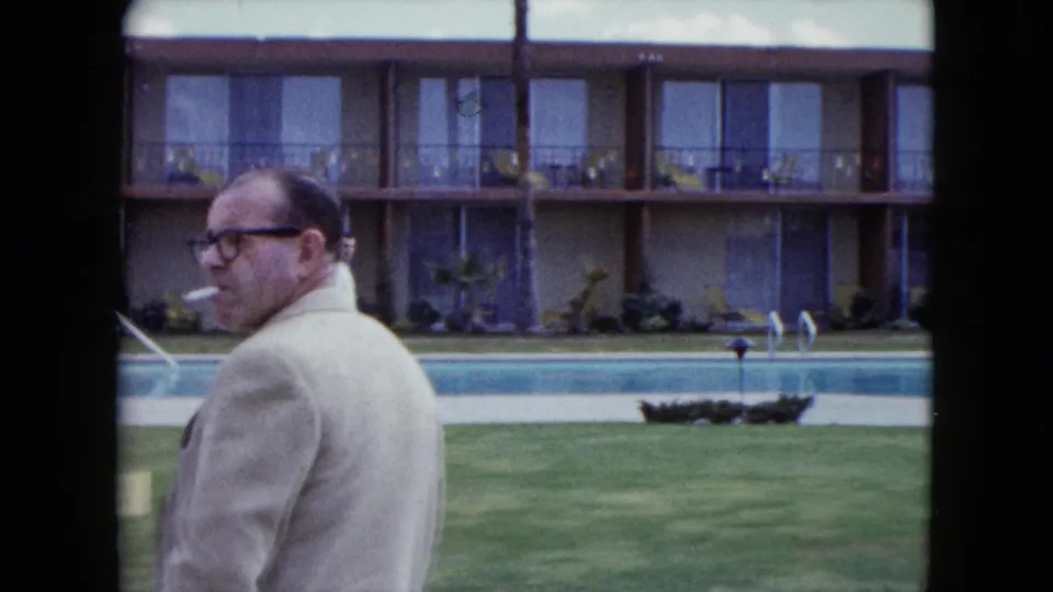 The smoking man moves partly out of frame in this 1959 Nevada motel pool view, leaving the pool, lawn, planter, and room balconies prominent.