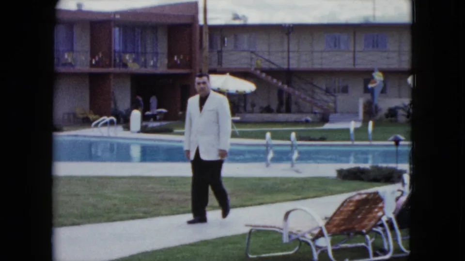 A closer poolside view shows the man walking past lounge chairs in a Nevada motel courtyard setting.