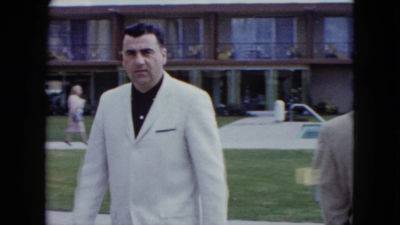 1959 Nevada resort scene with a man in a white jacket facing the camera beside a pool and lawn.