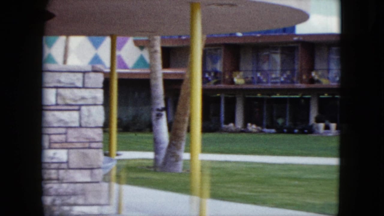 1959 Nevada resort exterior with lawn, palm trunks, yellow posts, stonework, and a mid-century facade seen from a home movie.