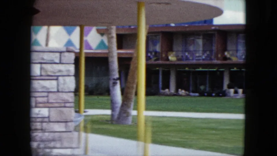 1959 Nevada resort exterior with lawn, palm trunks, yellow posts, stonework, and a mid-century facade seen from a home movie.