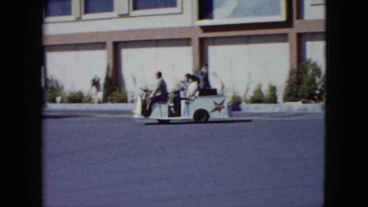 A white star-decorated shuttle cart carries several riders past a Nevada resort facade in 1959 home-movie footage.