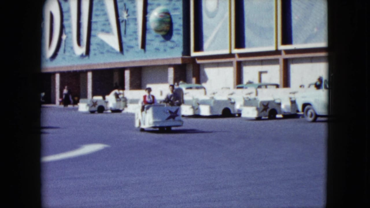The Stardust Hotel exterior fills the background while a small white cart with riders crosses the sunlit parking lot.