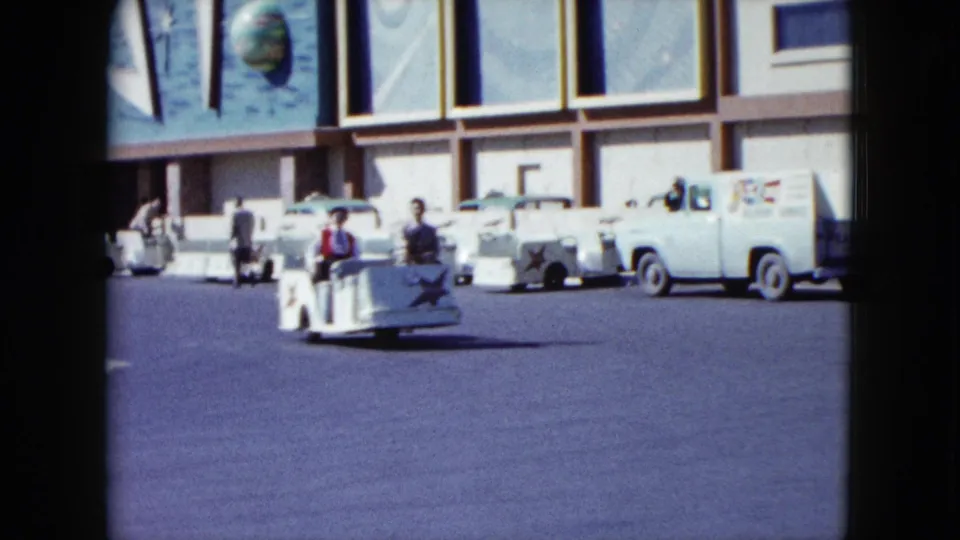 A closer 1959 frame shows riders in small white Stardust carts moving past parked mid-century cars outside the hotel.