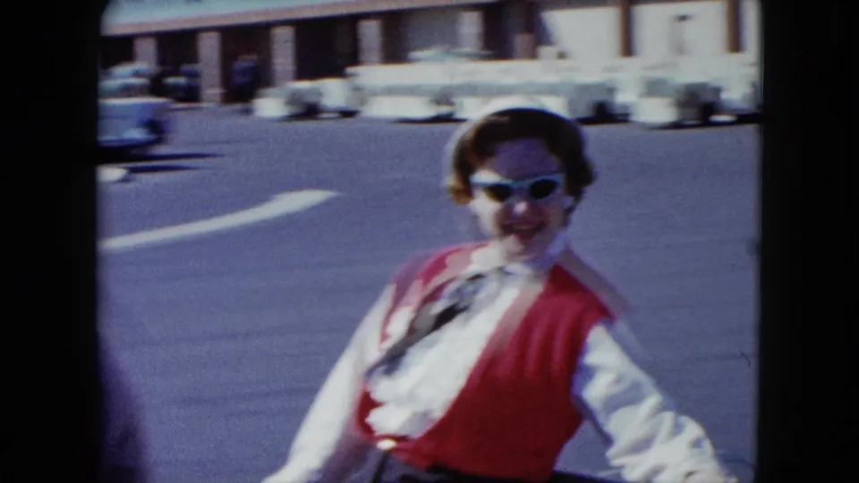 A close view shows the woman passenger smiling in sunglasses and a red vest as the cart crosses the parking lot.
