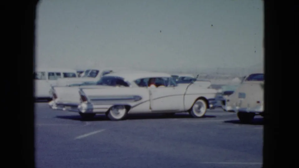 1959 Nevada home-movie view of a white finned sedan parked among other mid-century vehicles in bright daylight.