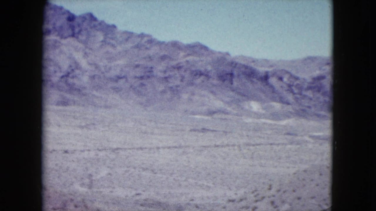 Wide Nevada desert view with rocky hills, dry open ground, sparse scrub, and pale sky in 1959 8mm footage.