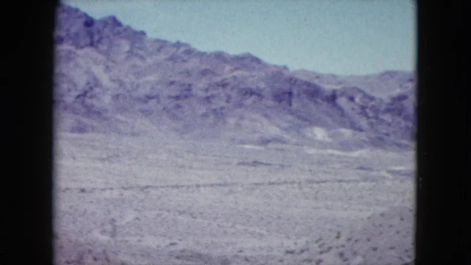 Wide Nevada desert view with rocky hills, dry open ground, sparse scrub, and pale sky in 1959 8mm footage.
