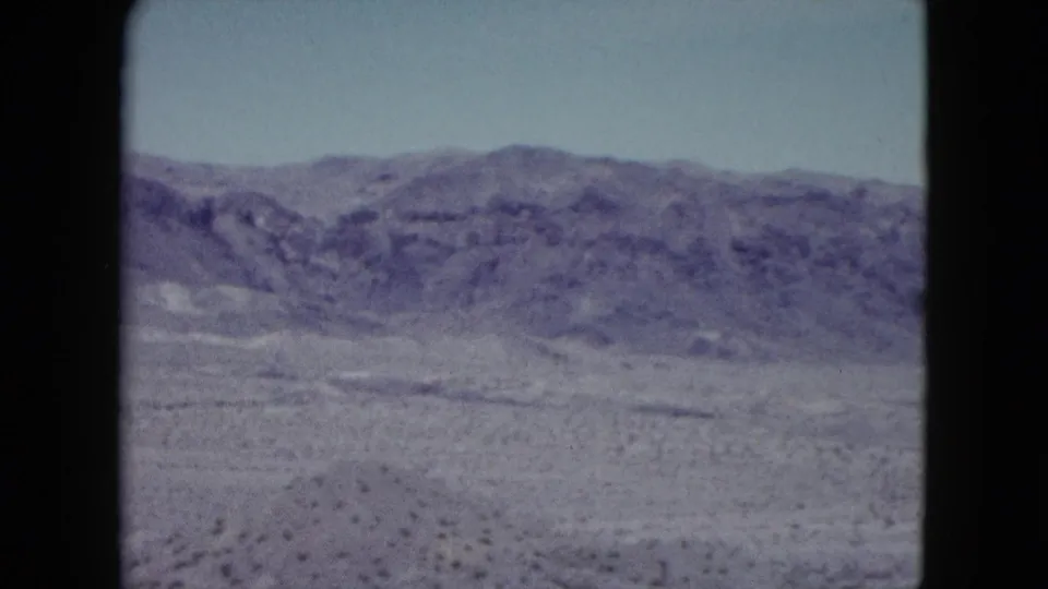 Wide 1959 Nevada desert view with low rocky hills, open arid ground, scattered scrub, and faded 8mm color.