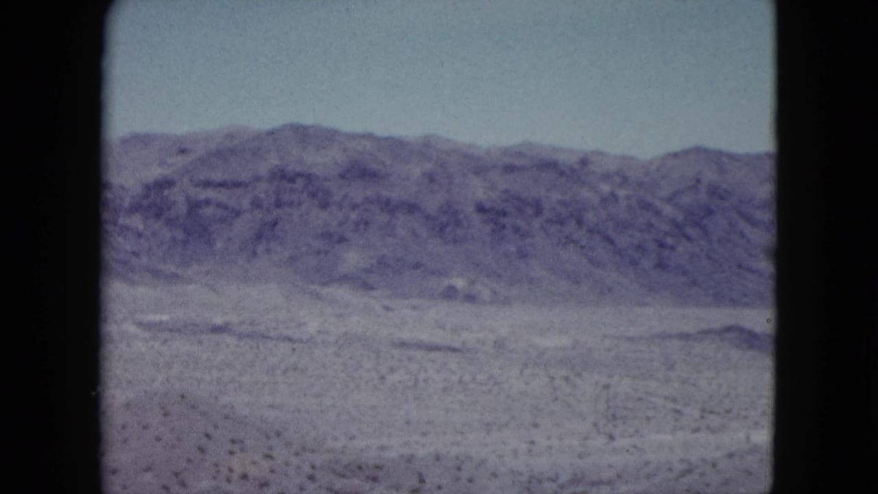 1959 Nevada 8mm frame showing a flat desert plain with sparse scrub and a long mountain ridge on the horizon.