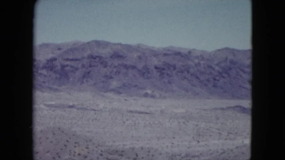 1959 Nevada 8mm frame showing a flat desert plain with sparse scrub and a long mountain ridge on the horizon.