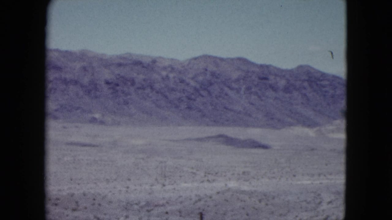 1959 Nevada home-movie view of rugged mountains across a muted desert basin, with aged color and black film edges.