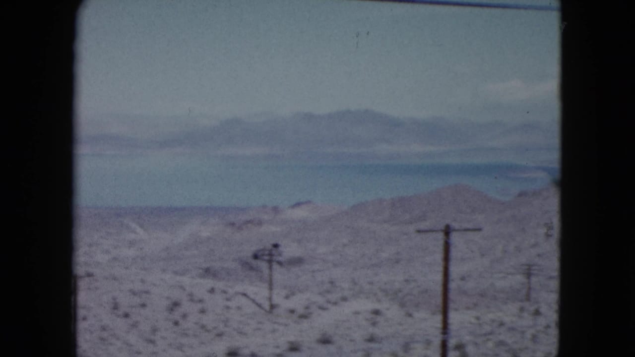 Desert hills with scattered shrubs, wooden telephone poles, distant mountains, and dark frame edges.