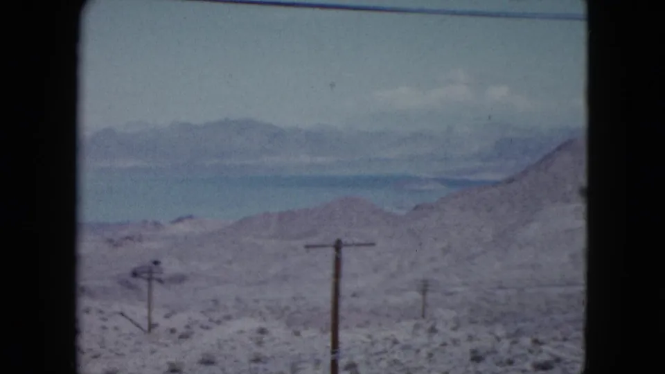 Mid-century Nevada desert footage showing telephone poles in open brushland with hazy mountains beyond.