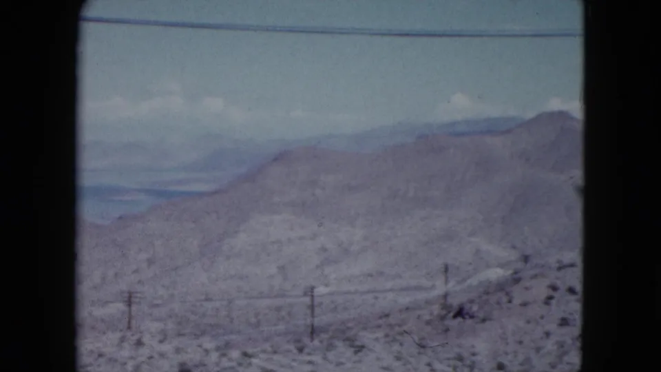Faded 8mm Nevada desert frame showing a sloped hillside, low brush, utility poles, and distant terrain.