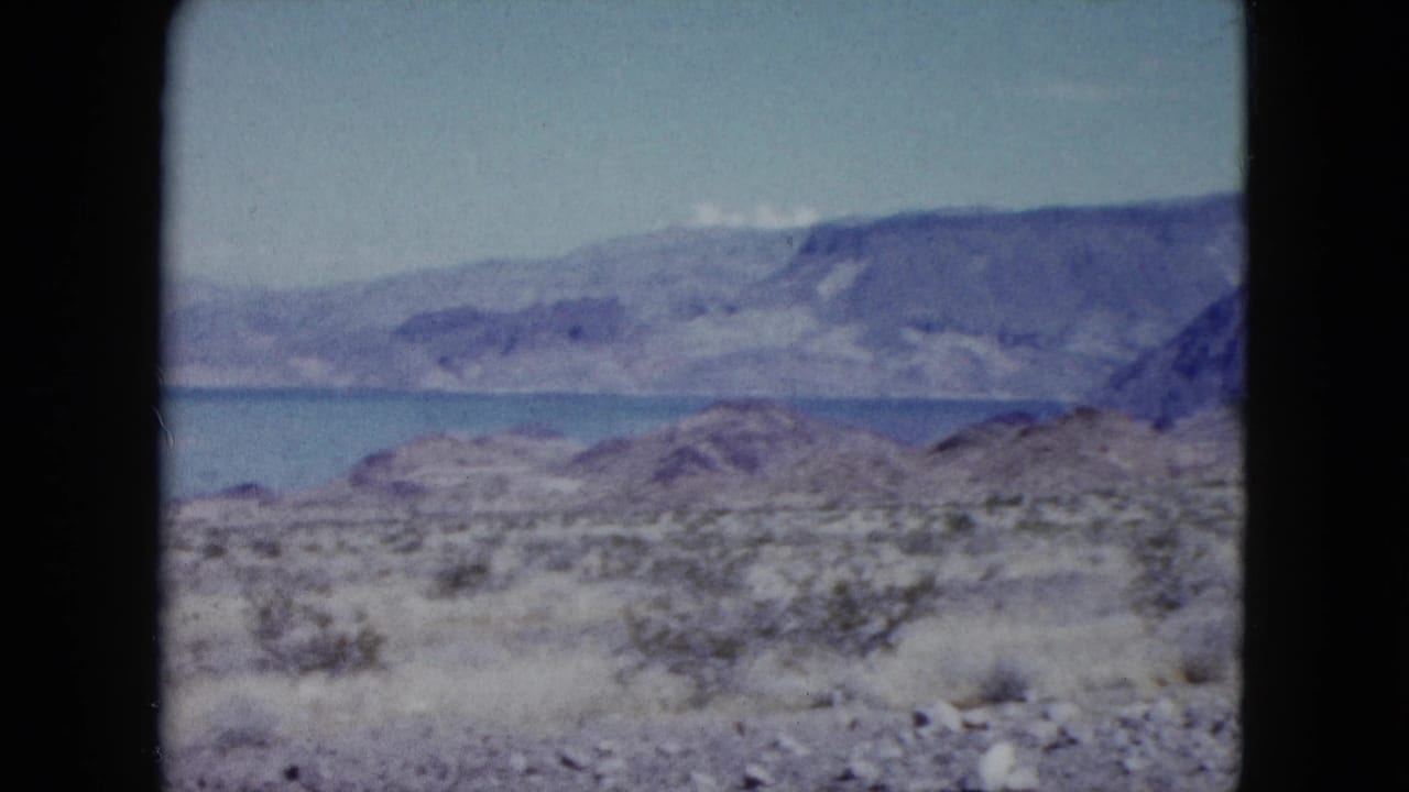 Rocky desert foreground opens to lake water and rugged mountain slopes.