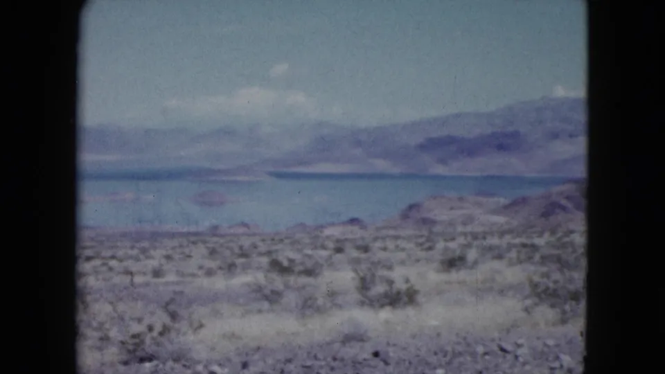 1959 Nevada 8mm view across desert brush toward a blue lake and hazy mountain range under scattered clouds.