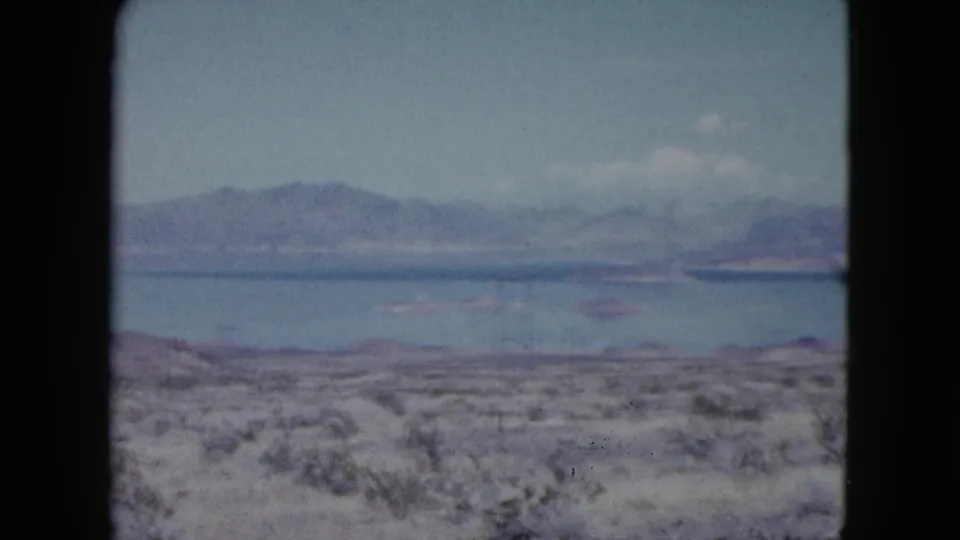 1959 Nevada 8mm frame showing a wider lake panorama, desert vegetation, distant islands or shoreline forms, and mountain ridges.