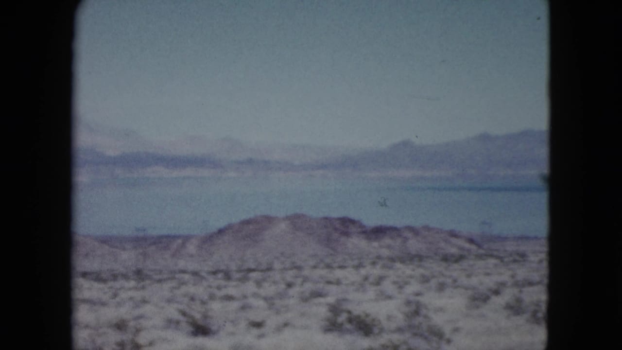 1959 Nevada landscape frame with a blue lake, hazy mountain ridge, and arid foreground brush.
