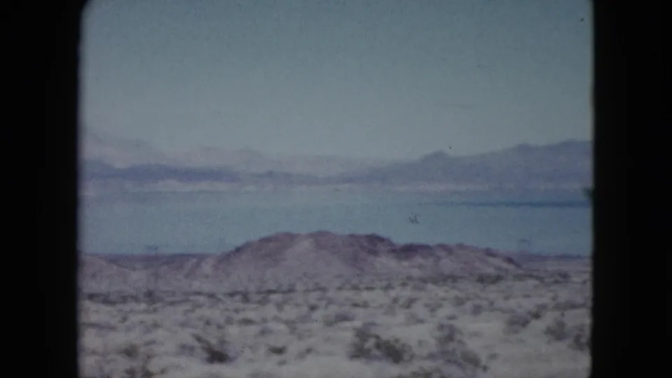 1959 Nevada landscape frame with a blue lake, hazy mountain ridge, and arid foreground brush.