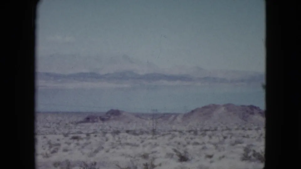 Soft 8mm Nevada view of scrubby desert land leading toward a lake and far mountain range.