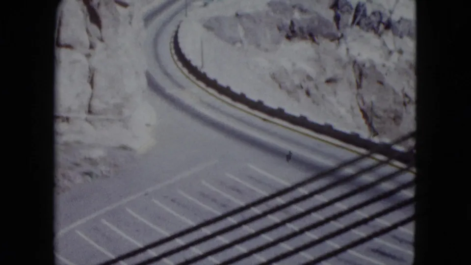 Winding paved road in rocky Nevada terrain, seen from above with lane markings, roadside edge, and dark foreground lines.