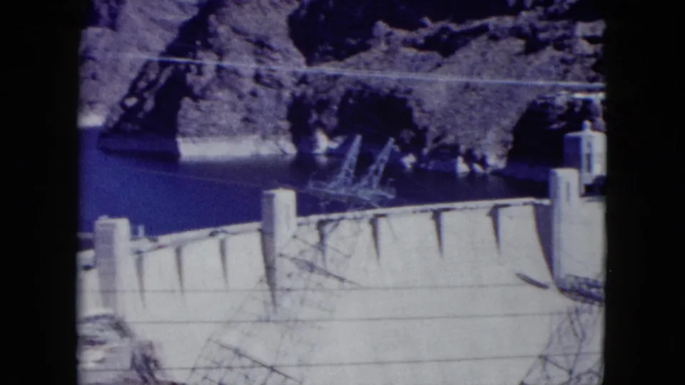 1959 Nevada home-movie frame of Hoover Dam, showing the concrete wall, Lake Mead, canyon rock, and adjacent structures.