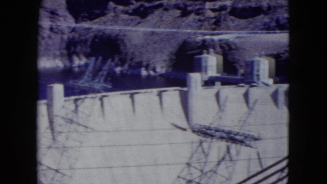 Hoover Dam concrete face with intake towers, canyon rock, and power-line shadows.