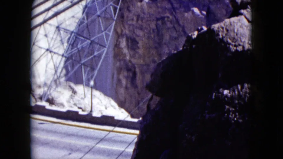 1959 Nevada home-movie view of Hoover Dam power infrastructure beside canyon rock and an empty road, framed by dark foreground shadow.
