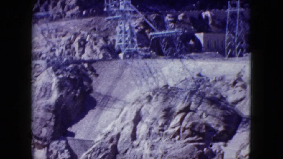 1959 Nevada footage showing power lines and utility towers set against rugged rock formations and dry ground.