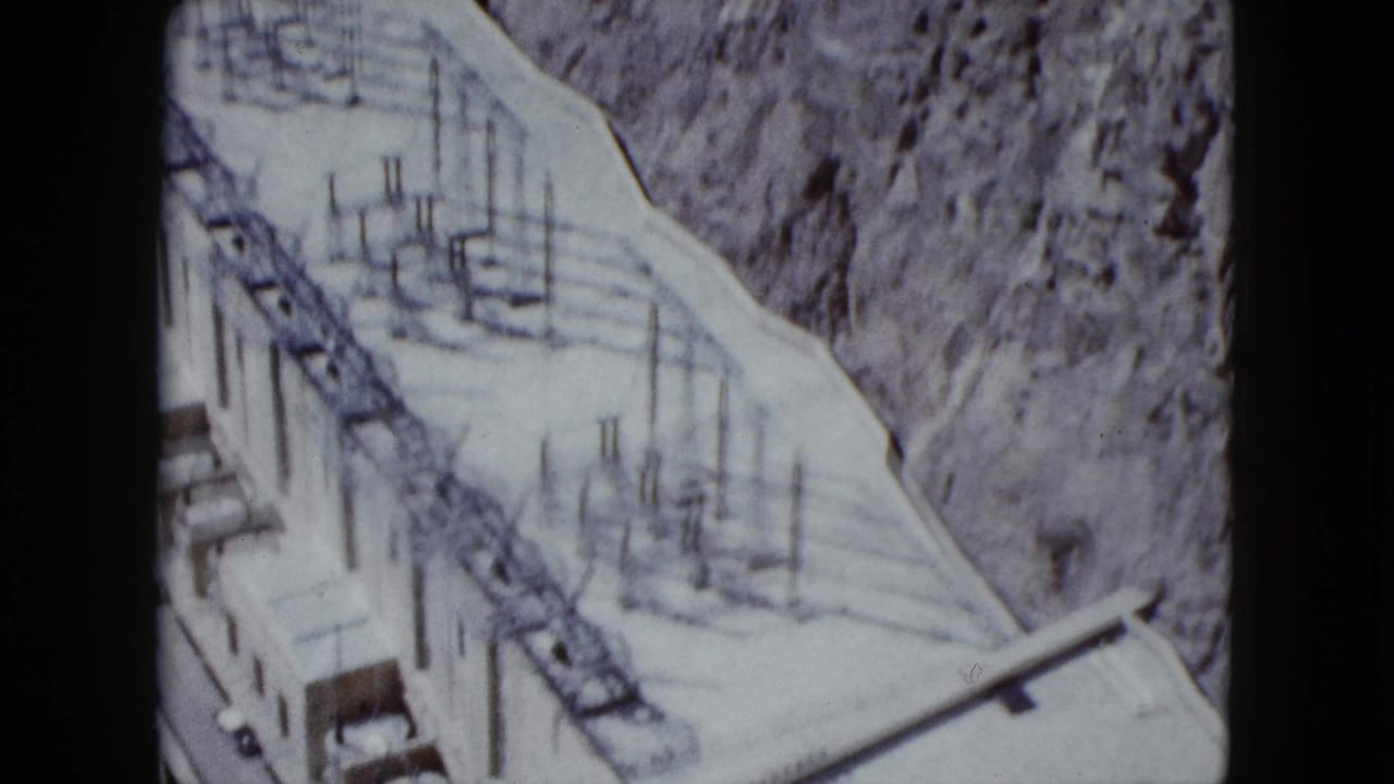 1959 Nevada 8mm frame showing concrete dam works, metal rods, and a rocky canyon edge from above.