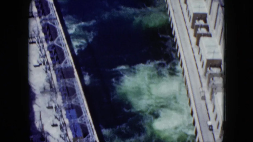 Color 8mm frame of Nevada dam construction with concrete sides, metal framework, and water turbulence below.