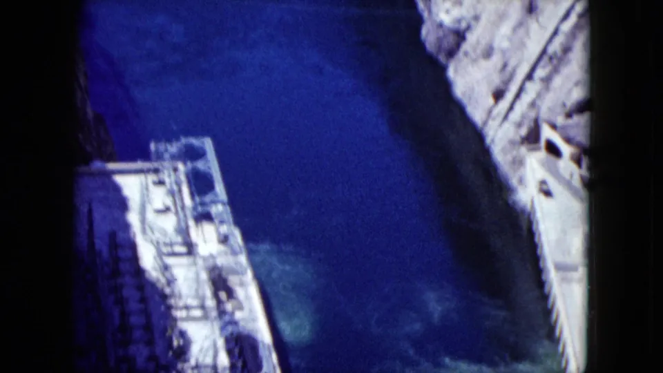 1959 Nevada dam-site frame showing deep blue water between concrete structures and canyon rock.