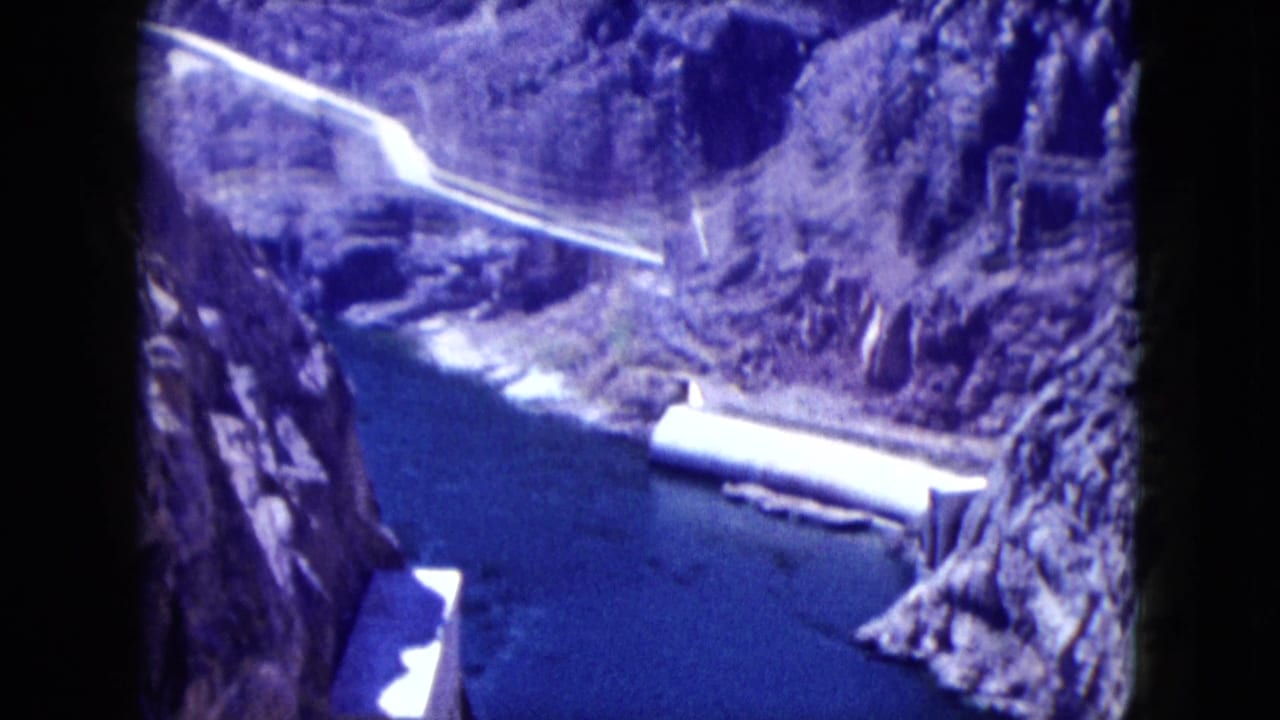 1959 Nevada canyon view showing blue water, pale pipeline or road, steep rock slopes, and concrete dam elements.