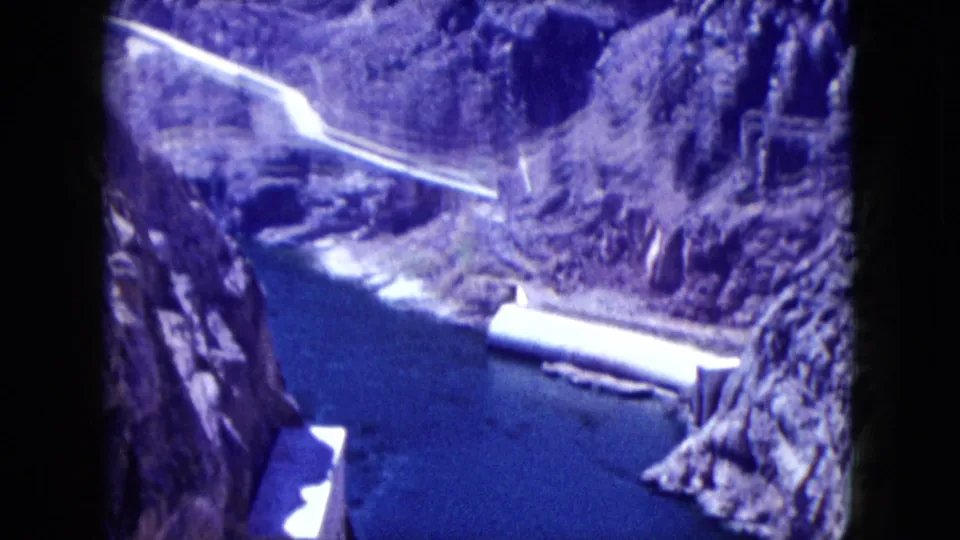 1959 Nevada canyon view showing blue water, pale pipeline or road, steep rock slopes, and concrete dam elements.