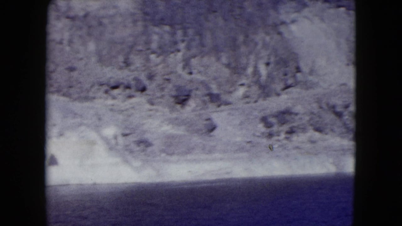 1959 Nevada 8mm frame showing pale rocky mountains dropping toward a deep blue lake or reservoir.