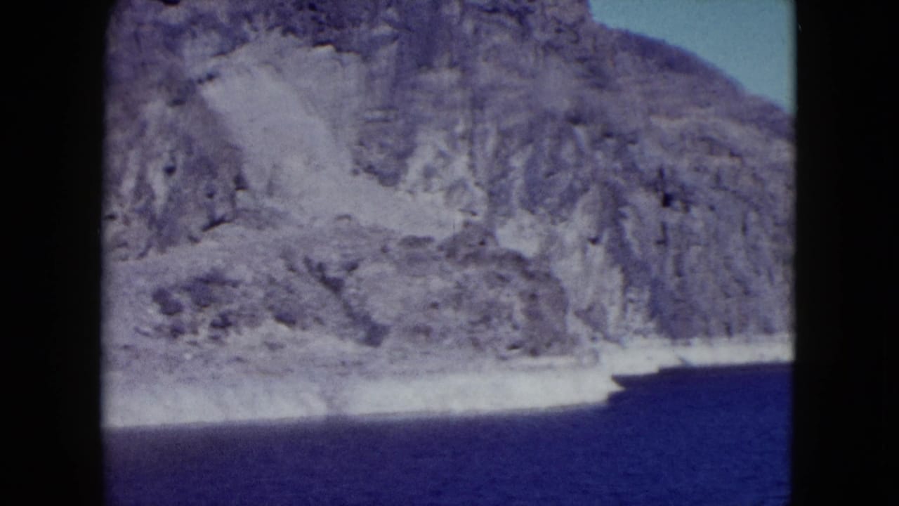 Steep rocky shoreline and blue water seen through a rounded film gate.