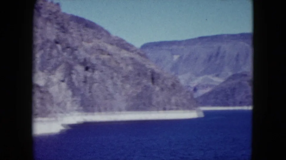 1959 Nevada 8mm frame with layered rocky mountains, a distant ridge, and blue lake or reservoir water.