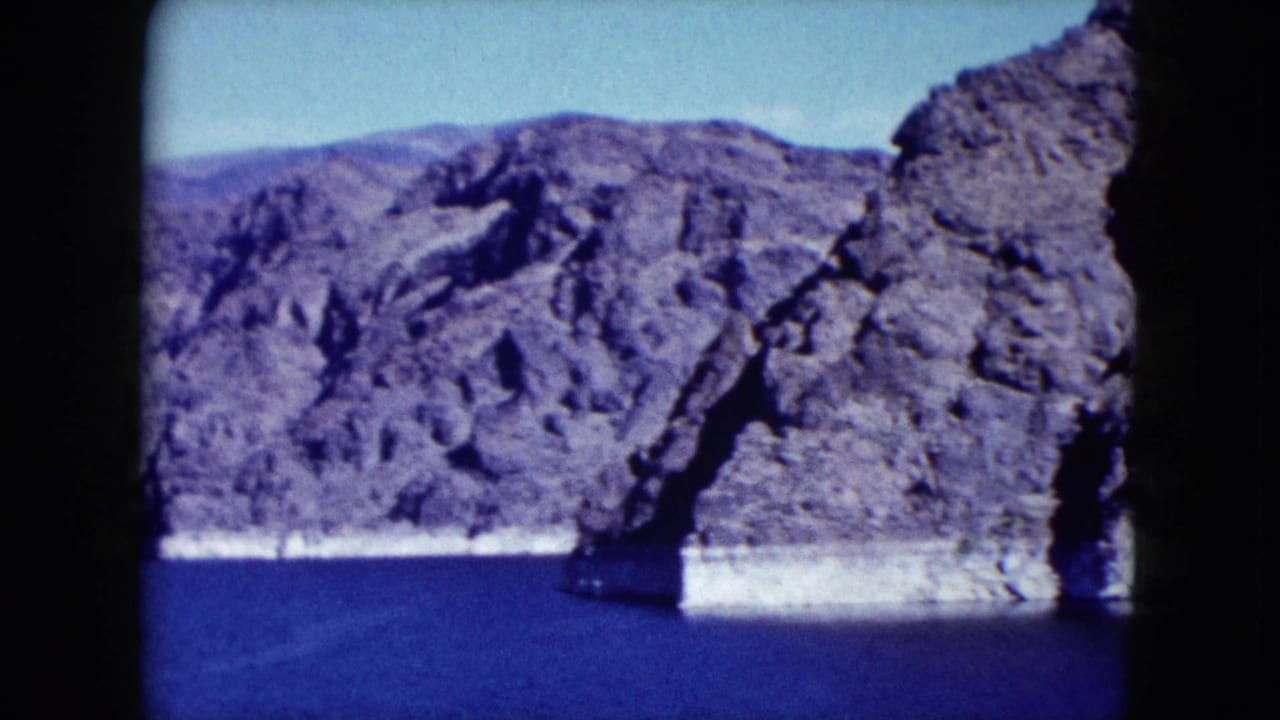 Rugged cliff face rising from blue water with pale shoreline at the base.